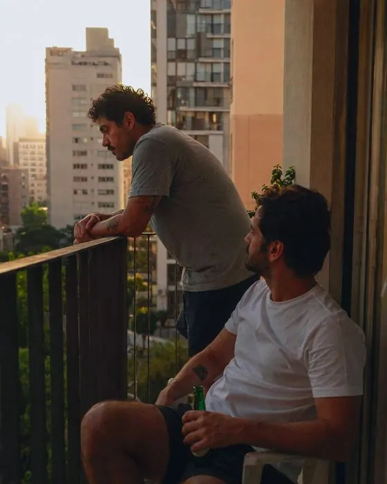 Dani e Rafa conversam na varanda, com a cidade ao fundo.